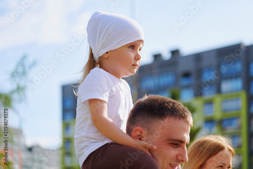 Konstfotografi Cute little girl enjoying a piggyback ride on her father's shoulders outdoors, exploring the city on a sunny day
