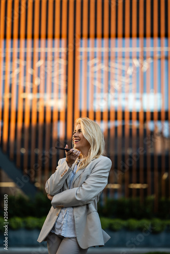 Fotografía Woman talking on phone using voice assistant outside office
