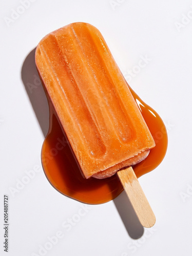 Melting Orange Ice Pop Popsicle with Liquid Puddle on White Background