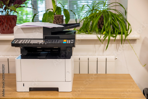 Modern laser printer machine on wooden desk in corporate office. Concept: office printing
