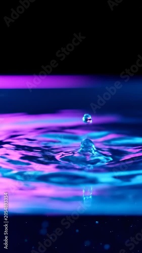 Water drop impact creating ripples and splash in neon purple and blue lighting, high speed photography