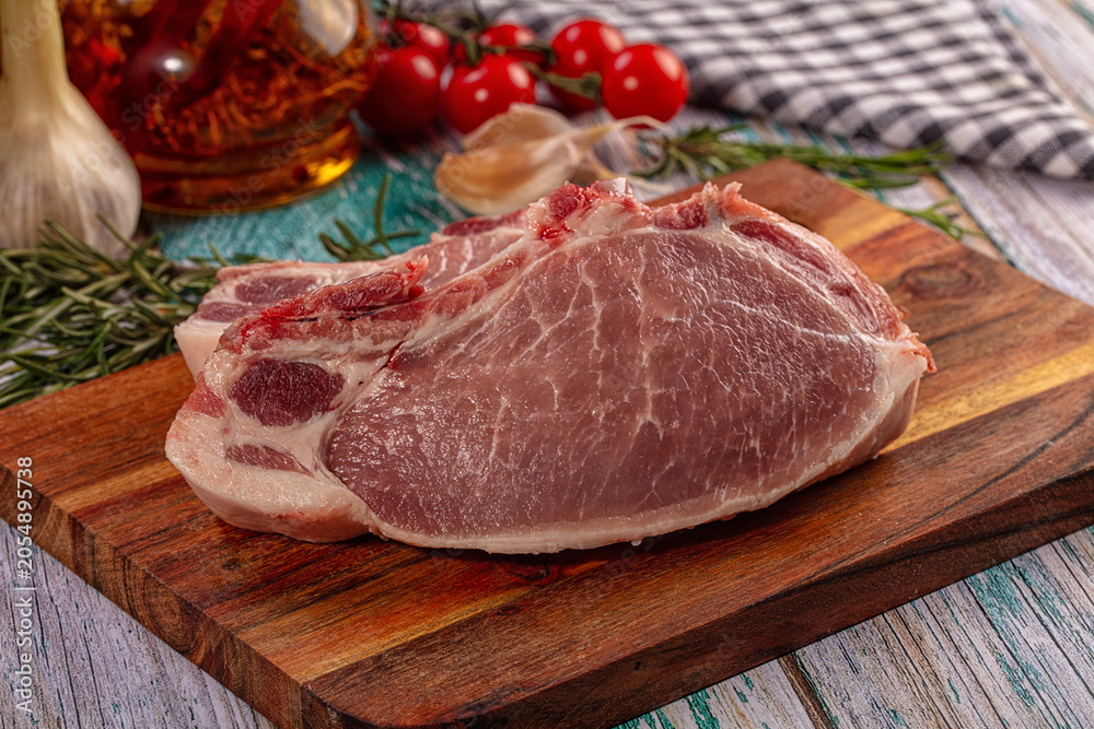 Fototapeta premium Raw pork steak on wooden board with rosemary and garlic
