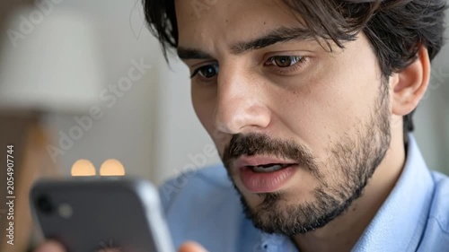A focused young man looking intently at his mobile device screen
