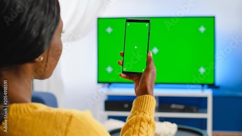 A woman holds a smartphone with a green screen at home