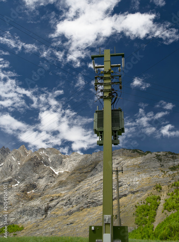 Low-voltage electricity distribution pole with transformer and insulators against blue sky, Switzerland