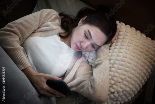 Konstfotografi Young woman with insomnia lying on sofa at night scrolling phone looking tired a