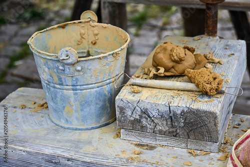 Supplies for clay modeling, including a bucket, modeling tool, and a sponge on a wooden plank, creative activity as a craft profession or a hobby, selected focus