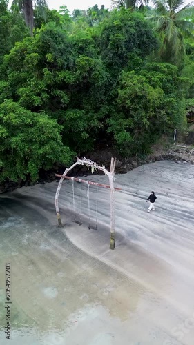 Moslem asian woman person enjoys a relaxing moment on a wooden swing at the beach in Weh island Sabang Indonesia, overlooking the ocean and the horizon on a sunny day.  Travel at the resort
