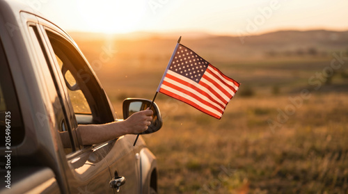 American flag waving from vehicle window during scenic countryside sunset drive, patriotic travel concept celebrating USA Independence Day, freedom, adventure and national pride