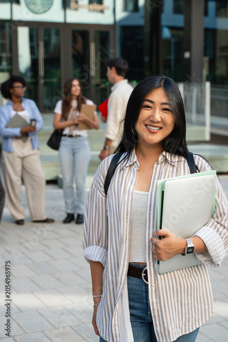 Asian female University student smiling at camera standing in front college entrance