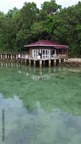 aerial drone pull away shot of a young romantic couple at a tropical beach resort with overwater bungalow. Luxury overwater villas on blue lagoon in Weh island, Sabang Aceh, Indonesia
