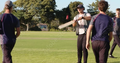 Diverse friends bowling ball to batsman tapping cricket bat, practicing batting in park