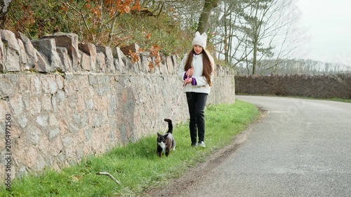 Girl walking with black and white cat on leash along quiet road, pet companionship moment. Child guiding small feline forward, relaxed pace, everyday activity with domestic animal. Kid strolling with