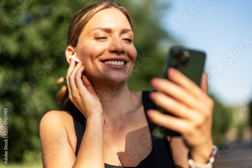 Woman, fitness and phone with earphones in town for break, streaming service or smile for audio. Gen z girl, runner and listen to music on app, happy and rest with smartphone for exercise