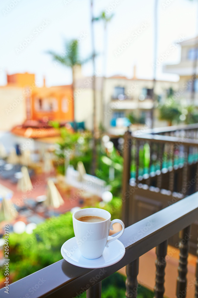 Naklejka premium Cup of coffee on a hotel balcony overlooking a swimming pool and tropical courtyard in Tenerife, Canary Islands, Spain.