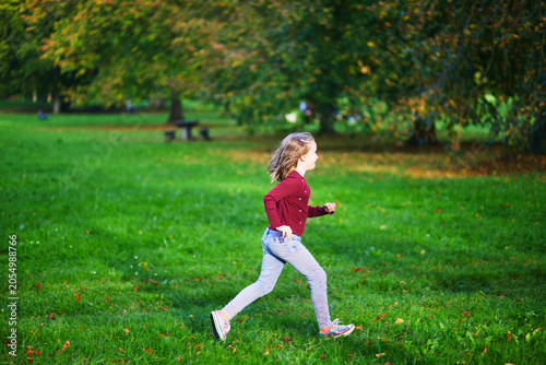 Young girl running across green grass in a park, enjoying outdoor play