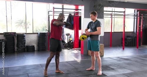 African american trainer slipping mitts at gym calling cues as trainee throwing punches