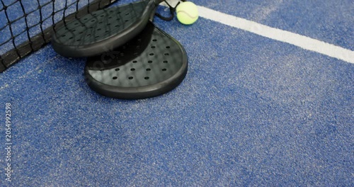 Camera tilting upward revealing two padel rackets resting on court beside black net for match