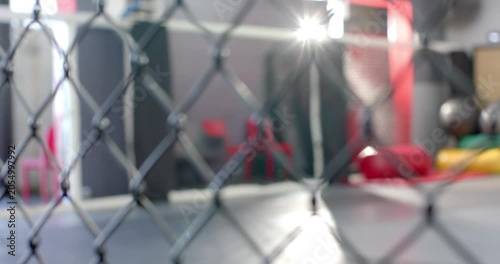 Camera is pulling focus from chain-link fence to reveal mats and hanging bags for martial arts