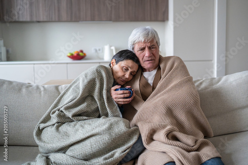 Canvastavla Upset senior man and woman covered in plaids sitting on sofa suffering from flu