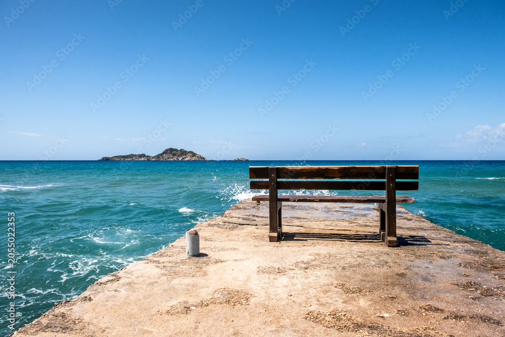 Fototapeta premium Bench on a stone pier with blue sea and sky background. Copyspace