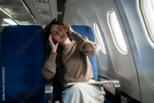 Tableau sur toile Tired young woman sitting by an airplane window, rubbing her forehead during a flight