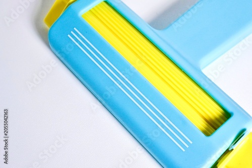Fotografi Close up blue and yellow paper crimper art and craft tool with manual roller isolated on horizontal white background