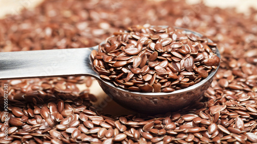Flaxseed in metal spoon close up with healthy brown seeds scattered on surface