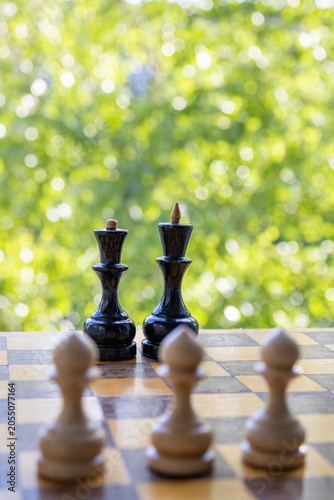 Fotografie Black chess king and queen pieces stand in focus behind blurred white pawns, symbolizing competition, strategic leadership, and different business teams