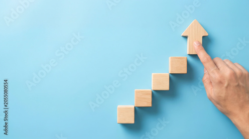 Hand moving wooden arrow block upward on stair steps showing business growth