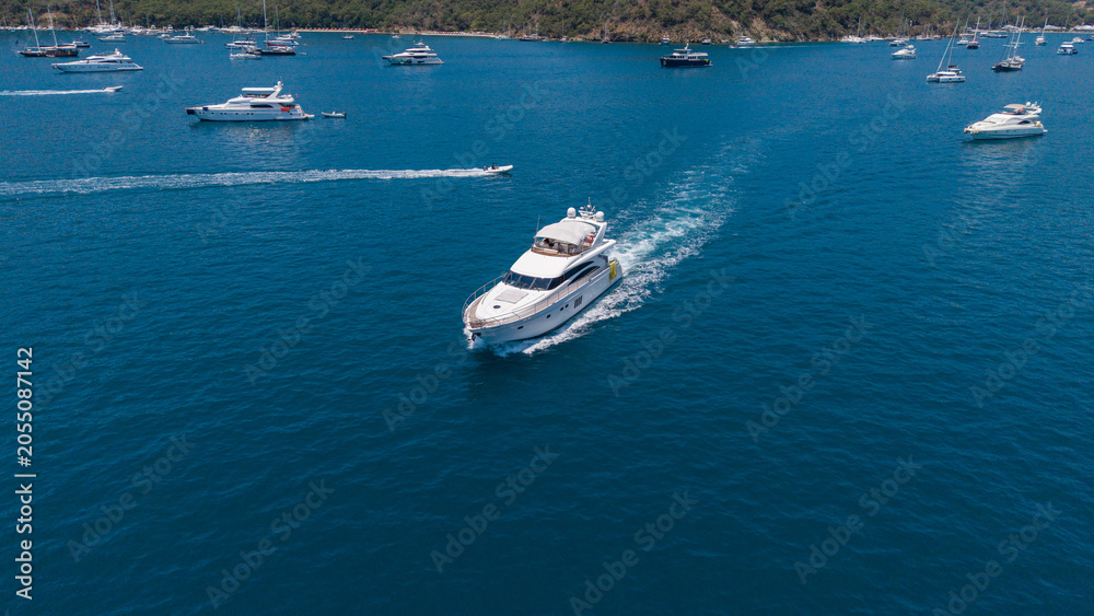 Fototapeta premium Luxury Yacht Cruise: A sleek white yacht cuts through the deep blue ocean, leaving a wake of white foam as other boats dot the horizon under a clear sky.