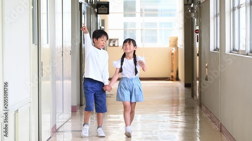 光の差し込む学校の廊下を手をつないで歩いてくる男女の小学生