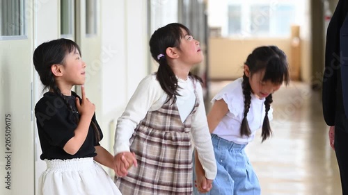 学校の廊下で先生を見上げて楽しく会話をする女子小学生たち