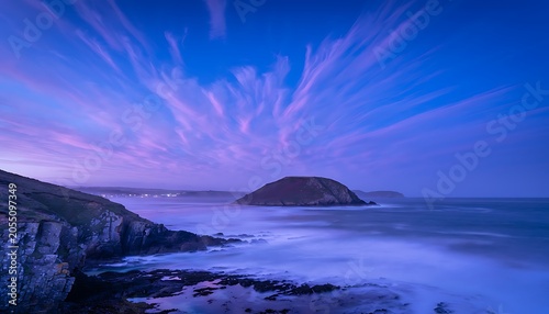 Feather-like cirrus clouds over a rocky coastline at twilight with a serene blue mood