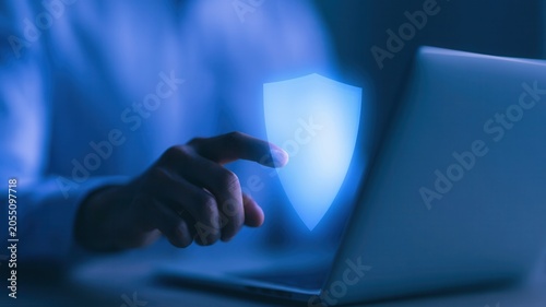 A close-up of a business hand touching a glowing digital data protection shield on a laptop screen, symbolizing secure network encryption.