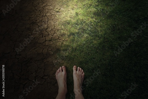 Bare feet standing between dry cracked earth and green grass background symbolizing environmental contrast for poster design