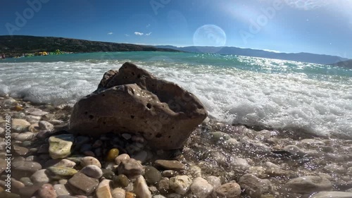 Rock on pebble beach with waves and bright summer sea