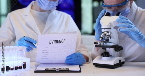 Scientist checks evidences list as colleague looks in microscope in lab. Female forensic experts conduct research for crime scene investigation