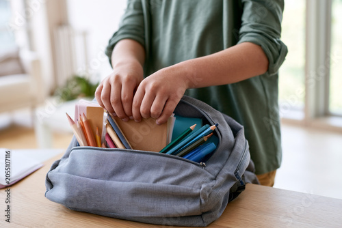 Close-up of child hands packing school supplies into backpack, soft daylight.