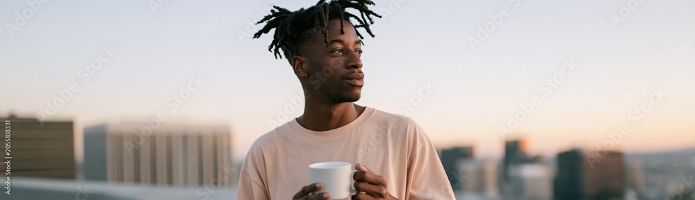 Naklejka premium Young man with dreadlocks holding white mug on rooftop at dusk background for lifestyle banner and social media design
