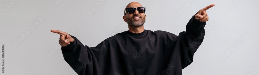 Obraz premium Confident man wearing sunglasses and black oversized sweatshirt pointing both directions for banner and social media background and promotional poster design