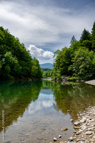 Vertical view of the emerald Kupa River with forest reflections and dramatic clouds creating a peaceful ecotourism scene along the Slovenia Croatia border