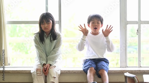 窓際に座って談笑する男女の小学生たち