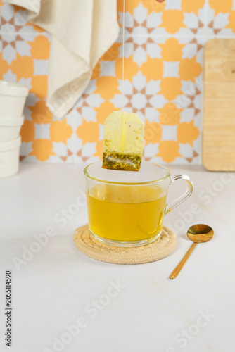 Hand dipping tea bag into clear glass mug of hot tea on white table