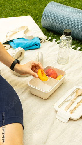 Woman eating fresh peaches from a lunchbox during a picnic after a workout