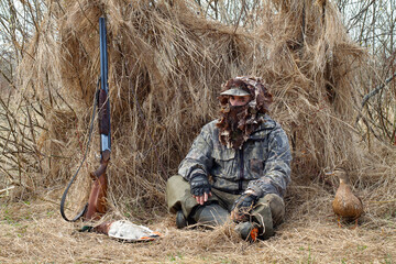 A hunter with a decoy duck sits in front of his duck blind