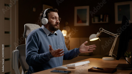 Fotografie Man in headphones looks at computer and shows with his gestures and appearance I