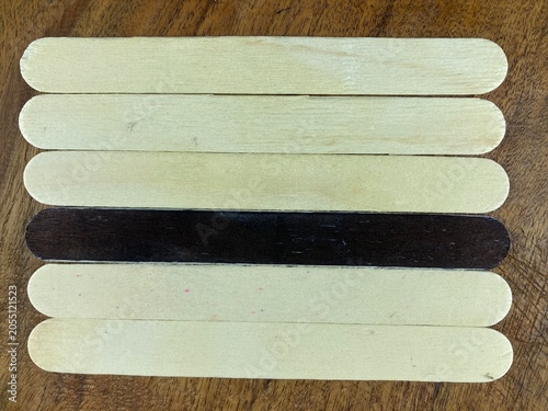 Unique dark tongue depressor among light ones, isolated wooden sticks 
