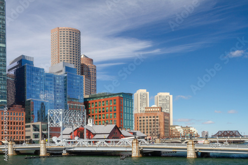 Modern glass skyscrapers and historic waterfront buildings create a striking skyline along Boston Harbor on a clear day in Massachusetts.