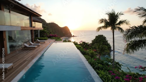 Serene infinity pool overlooking ocean with palm trees and modern house at sunset with warm tones.